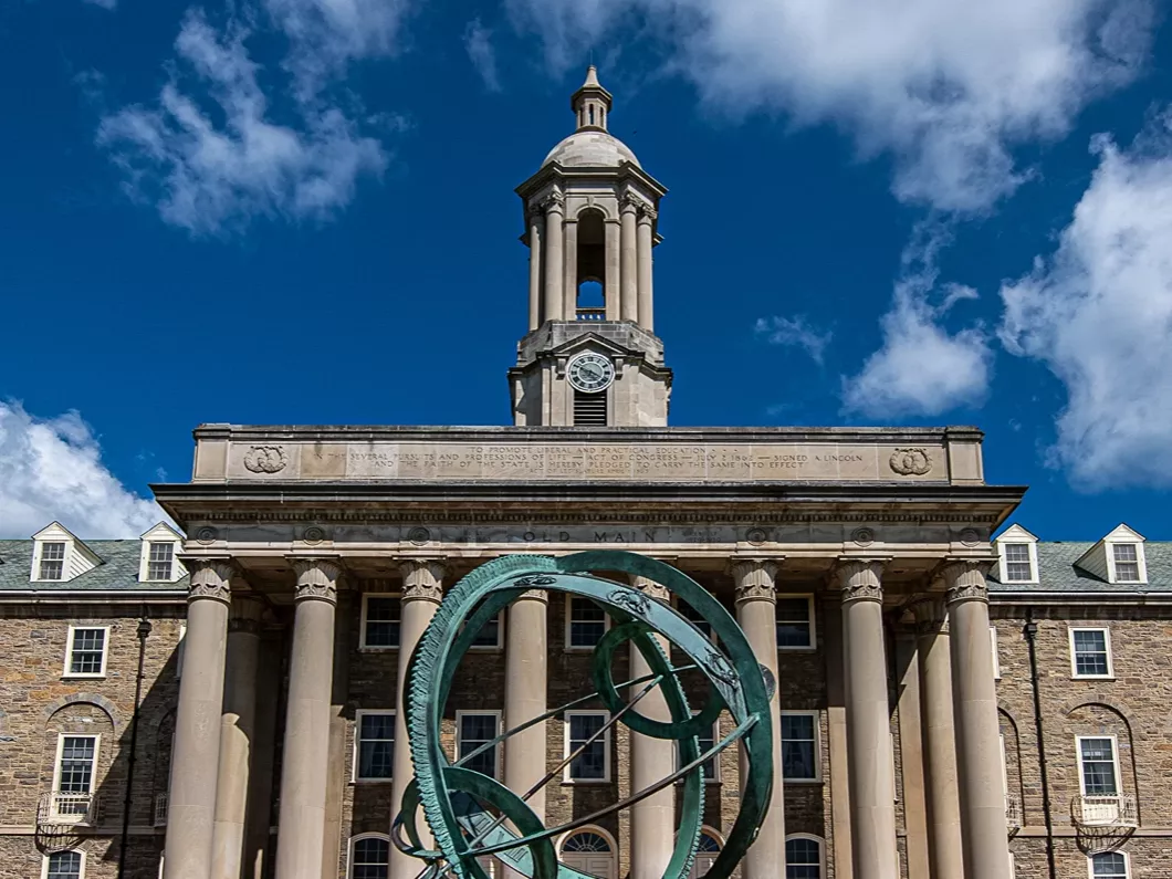 Old Main against a brilliant blue sky with the armilliary sphere in front